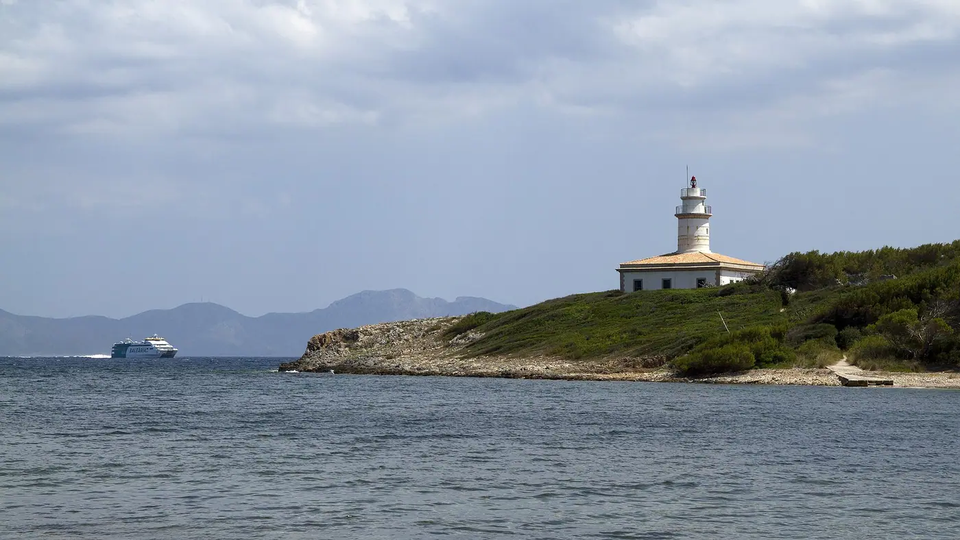 Le phare et l'îlot d'Alcanada vus depuis la plage, eau turquoise calme.