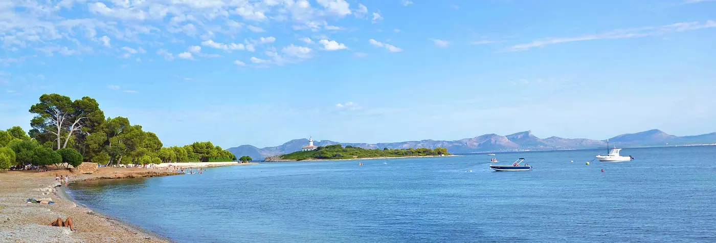 L'Illa d'Alcanada et son phare vus depuis la mer, petite barque au premier plan.