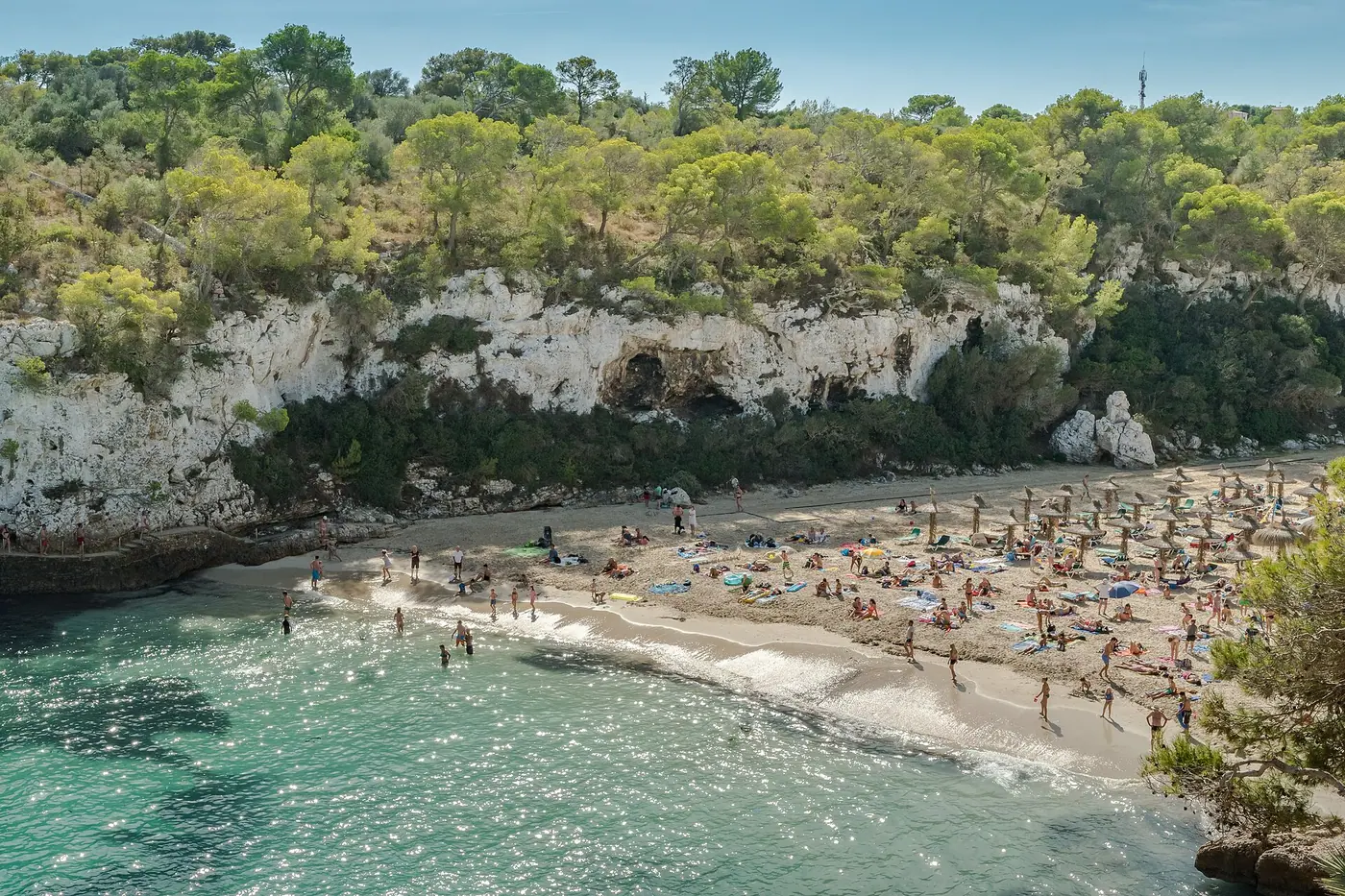 Vue aérienne de Cala Llombards, crique encaissée aux eaux turquoise entourée de pins.