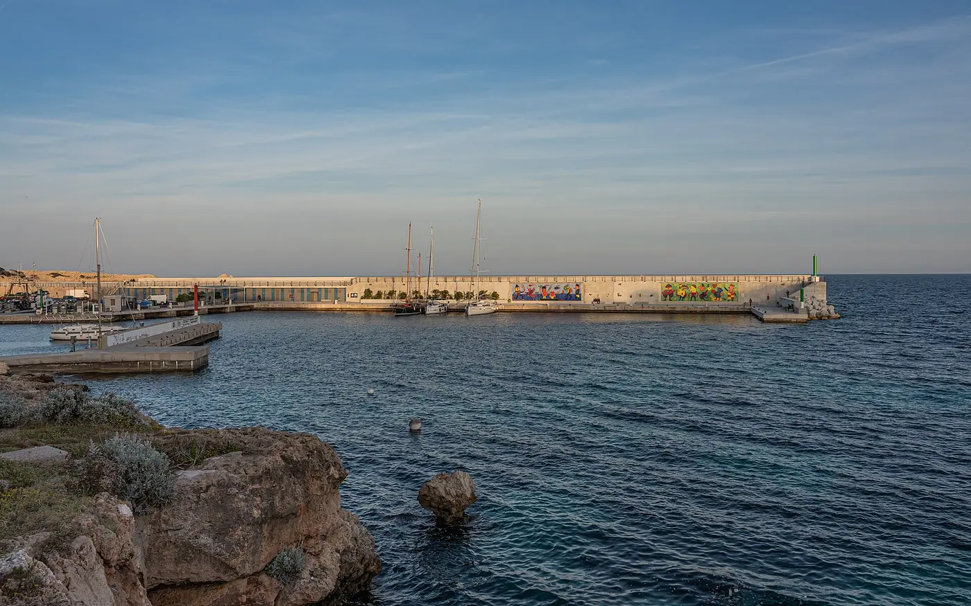 Entrée du port de Cala Rajada, phare et eau calme.