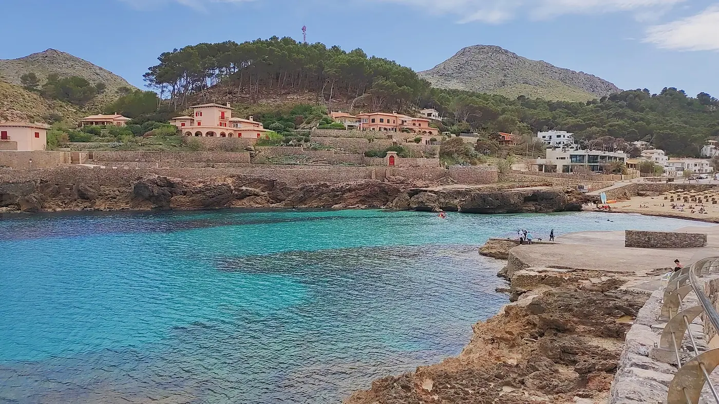Cala Molins nichée entre les falaises, village en arrière-plan.