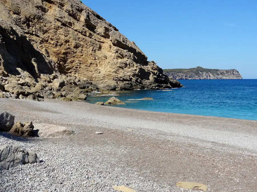 Anse isolée de Coll Baix, plage de galets encadrée de falaises.