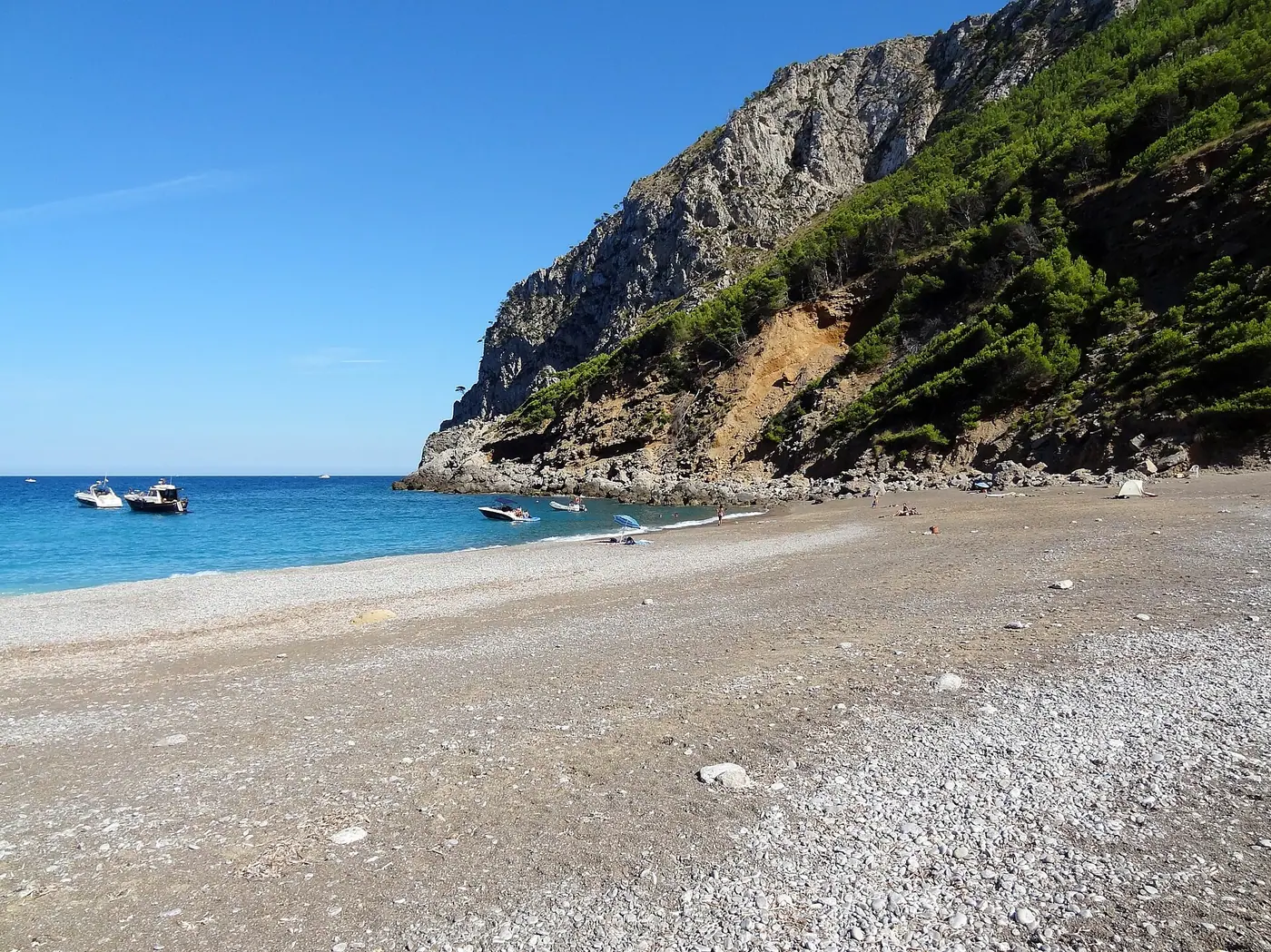 Crique de Coll Baix avec petites barques mouillées dans une eau limpide.