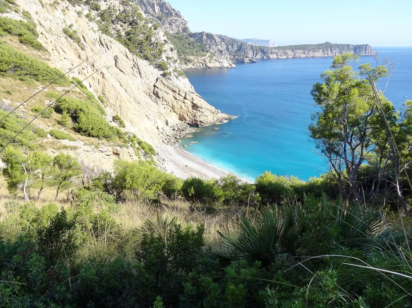Vue plongeante sur la crique turquoise de Coll Baix entourée de pins.