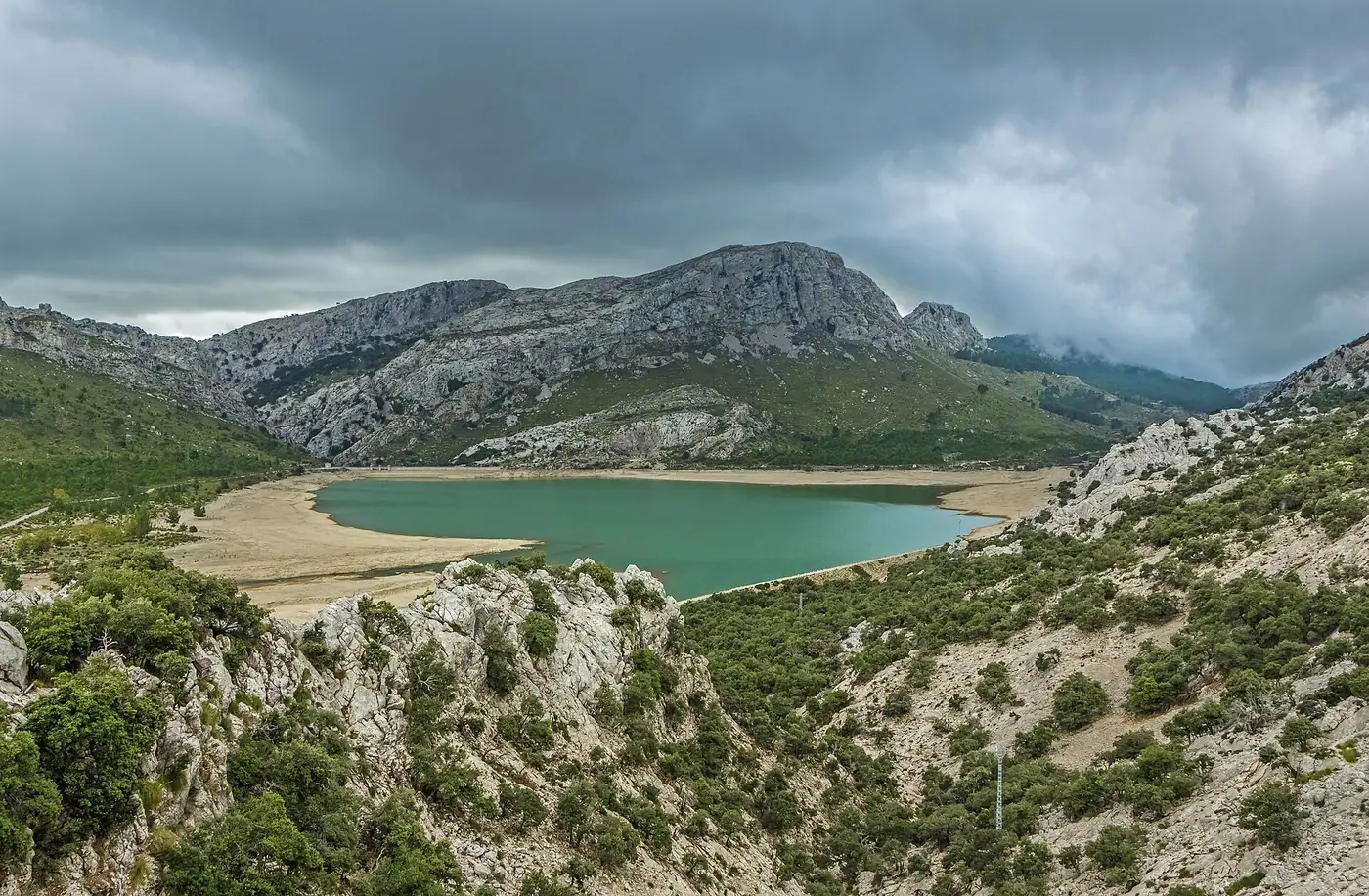Vue panoramique sur le lac de barrage de Cúber sous un ciel changeant.