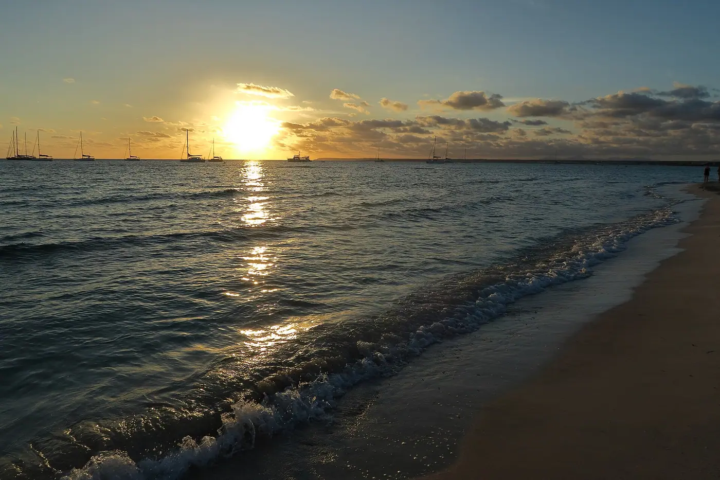 Coucher de soleil doré sur la plage d'Es Trenc et ses voiliers au mouillage.
