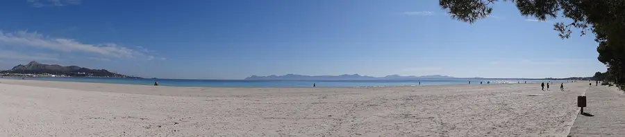 Vue large et minimaliste de la plage d'Alcúdia, sable fin et mer calme.