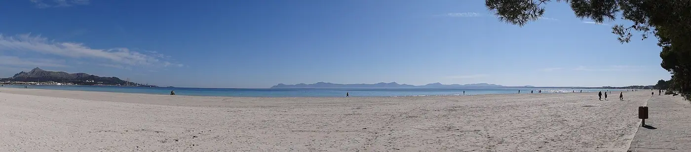 Vue large et minimaliste de la plage d'Alcúdia, sable fin et mer calme.